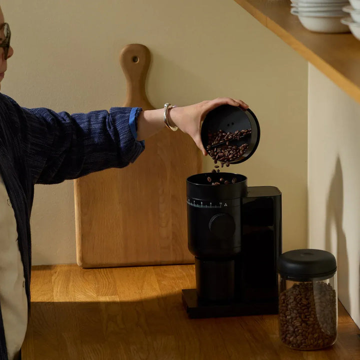 Fellow Opus 2 grinder — pouring whole beans into the hopper on a kitchen counter