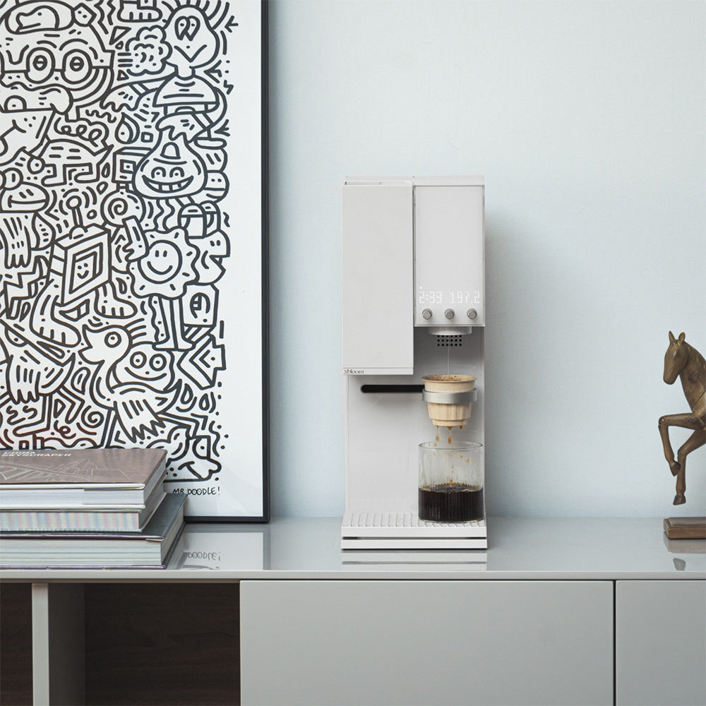 Moonlight White XBloom Studio Coffee Machine on a countertop with a decorative horse figure and abstract art in the background.