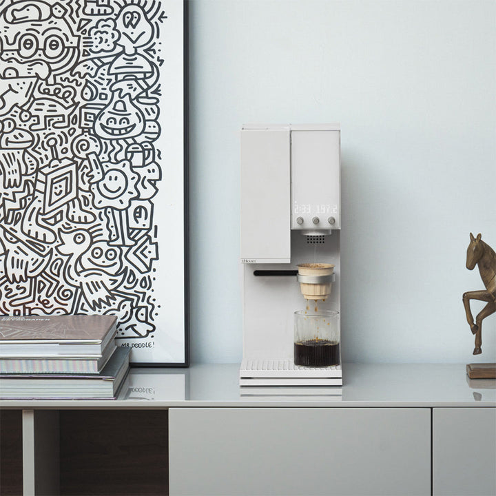Moonlight White XBloom Studio Coffee Machine on a countertop with a decorative horse figure and abstract art in the background.
