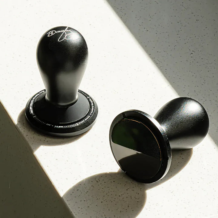 TIMEMORE FLOW tamper standing upright beside one lying on its side, showing the DLC-coated 58.5mm base