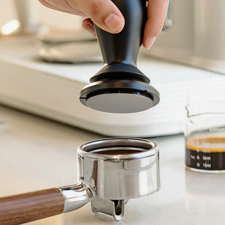 Barista using the TIMEMORE FLOW self-leveling tamper to tamp coffee grounds in a portafilter basket
