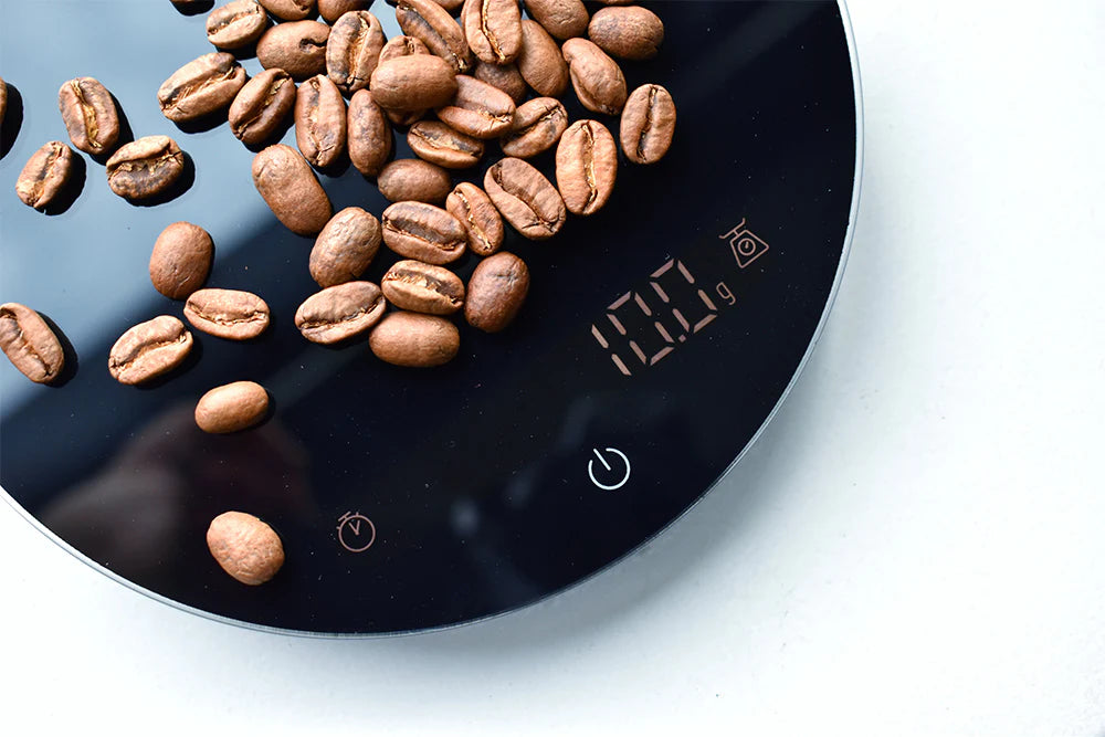 Coffee beans on a wilfa uniform plus digital kitchen scale displaying weight