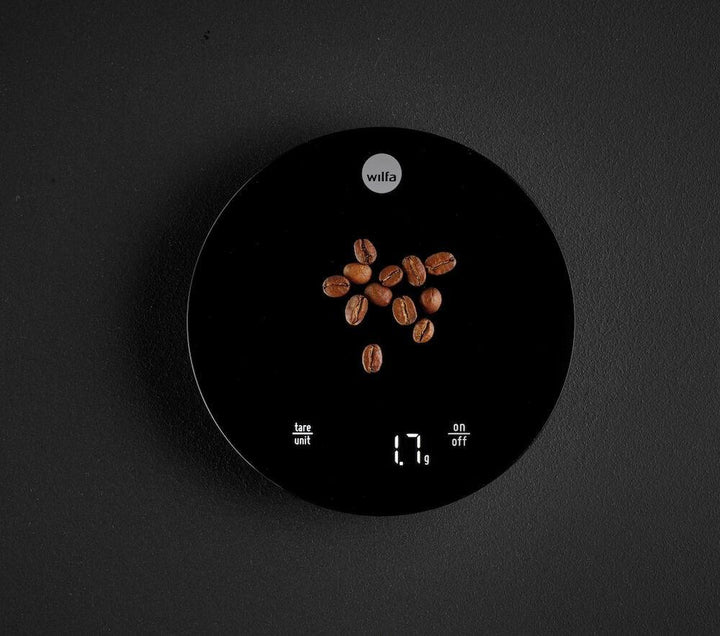 Black Wilfa Uniform Coffee and Kitchen Scale with a small amount of coffee beans on a black background