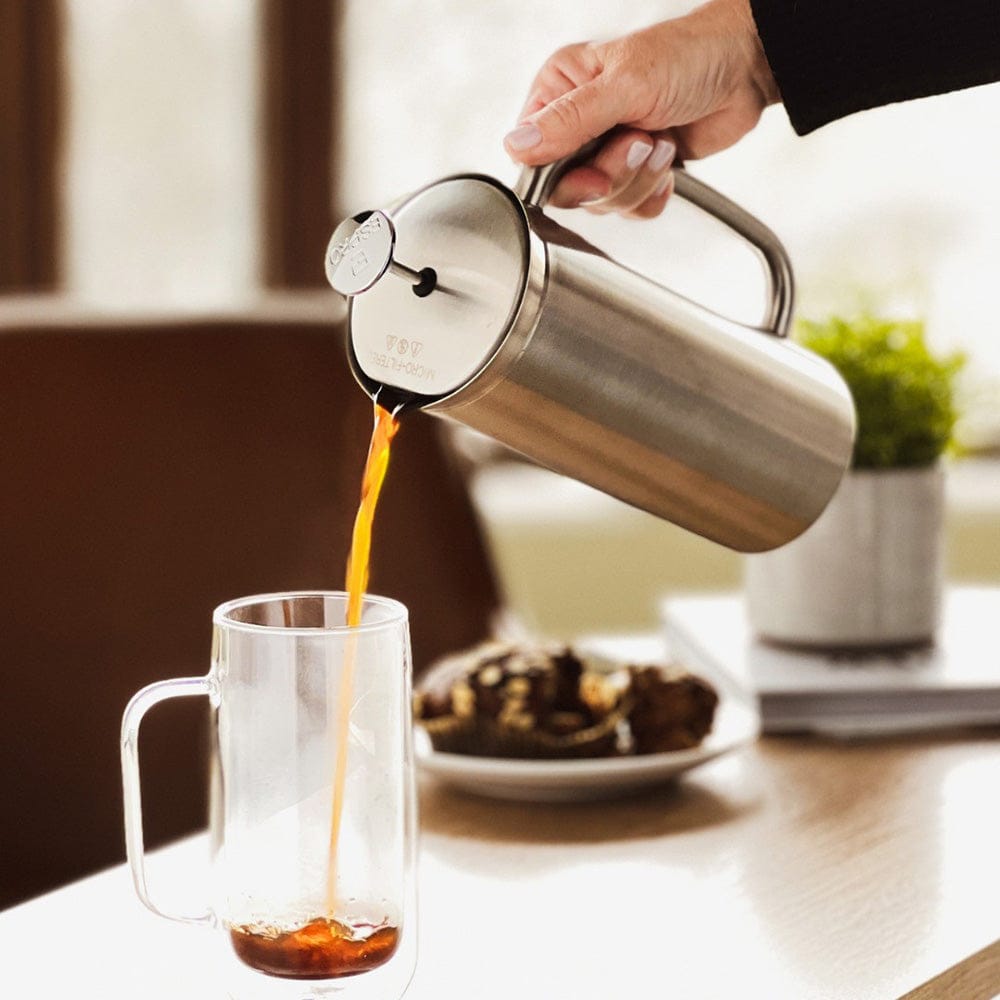 Person pouring coffee from a Brushed ESPRO P7 French Press Coffee Maker into a glass mug on a table.