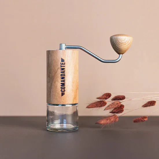 The Comandante C40 Nitro Blade Coffee Grinder MK4 in American Cherry with a glass base container on a beige background