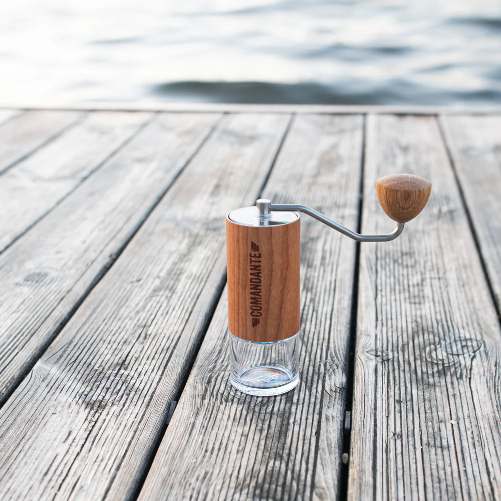 The Comandante C40 Nitro Blade Coffee Grinder MK4 in American Cherry on a wooden deck with water in the background