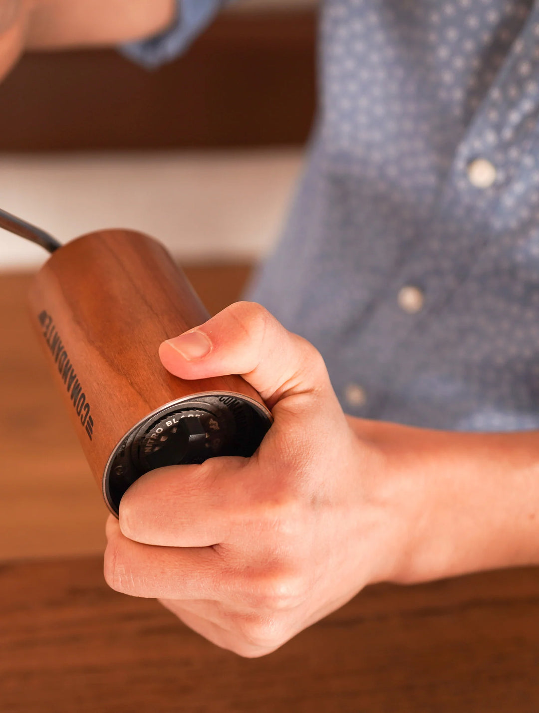 Hand holding a The Comandante C40 Nitro Blade Coffee Grinder MK4 in American Cherry with a blurred background
