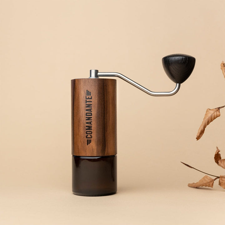 Comandante C40 Nitro Blade Coffee Grinder MK4 in Liquid Amber with a metal handle on a beige background