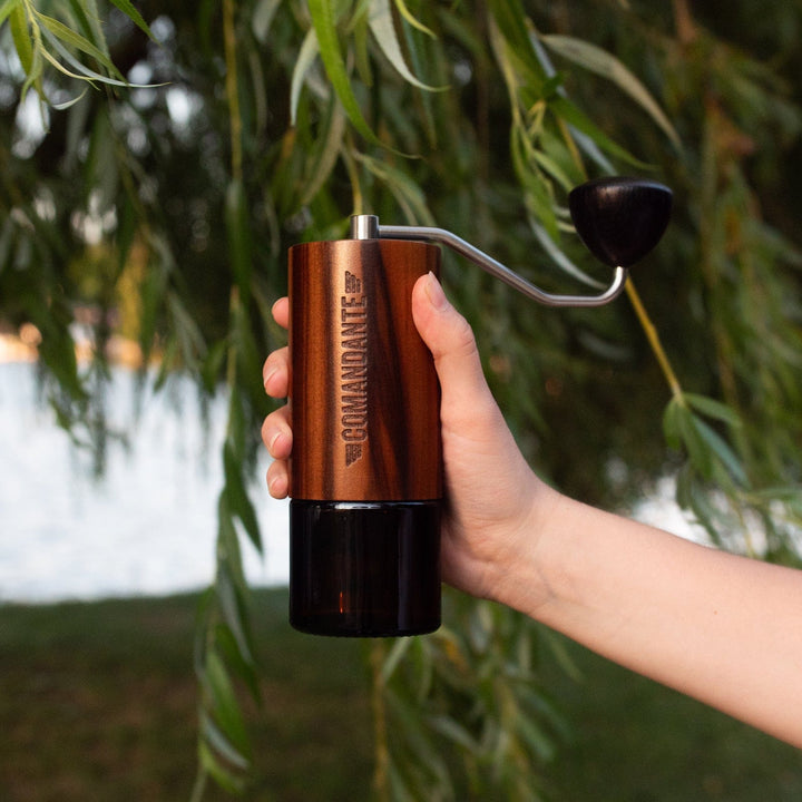 Hand holding a Comandante C40 Nitro Blade Coffee Grinder MK4 in Liquid Amber with a blurred natural background
