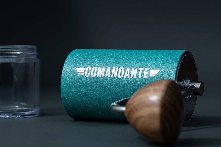 Comandante C40 Nitro Blade Coffee Grinder MK4 in Alpine Lagoon with 'Comandante' branding next to a clear glass coffee bean jar on a dark surface