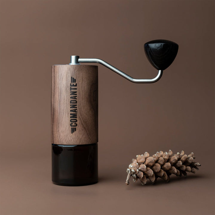 Comandante C40 Nitro Blade Coffee Grinder MK4 in Virginia Walnut with a pine cone on a brown background