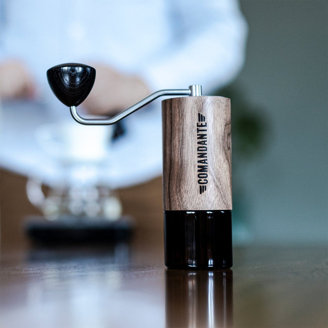 Comandante C40 Nitro Blade Coffee Grinder MK4 in Virginia Walnut  with black accents on a reflective surface, blurred background