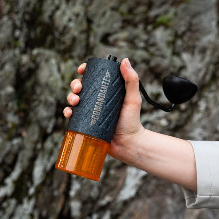 Hand holding a Comandante C60 Baracuda Coffee Grinder in Nautilus Blue against a natural background