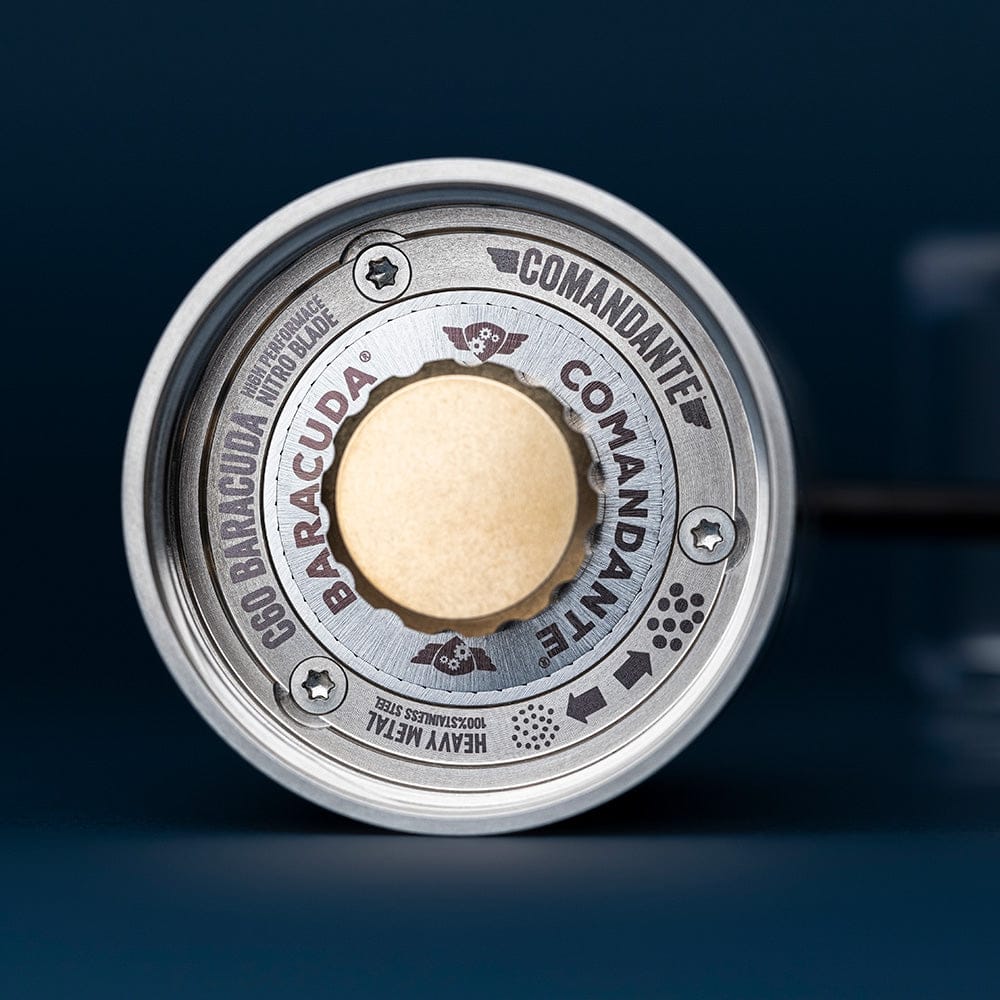 Close-up of the underside of the Comandante C60 Baracuda Coffee Grinder in Velvet Steel with 'Comandante Baracuda' branding on a dark background