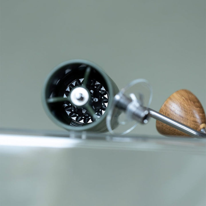 Close-up of a wooden-handled Comandante X25 Trailmaster Coffee Grinder in Forest Green on a neutral background