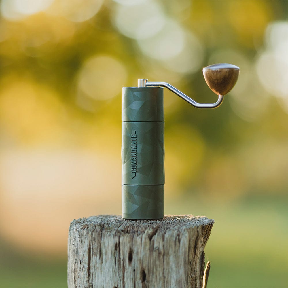 Comandante X25 Trailmaster Coffee Grinder in Forest Green on a wooden stump with a blurred natural background