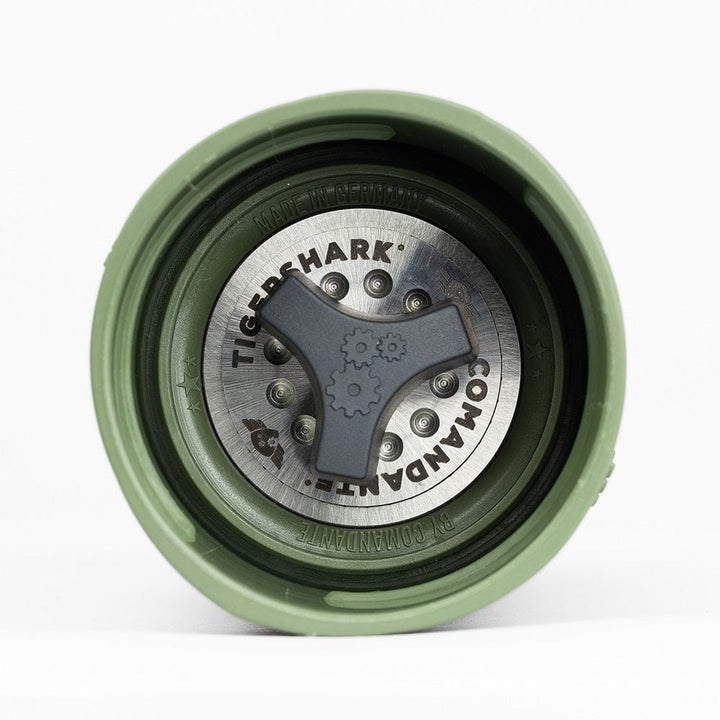 Close-up of the underside of a Comandante X25 Trailmaster Coffee Grinder in Forest Green with a metallic 'Comandante' logo on a white background
