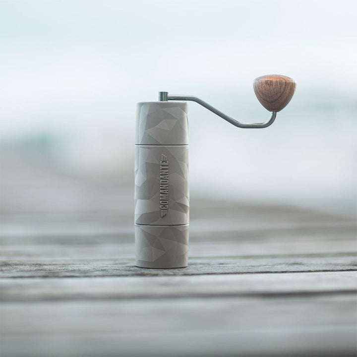 Comandante X25 Trailmaster Dune Coffee Grinder with a wooden handle on a wooden surface