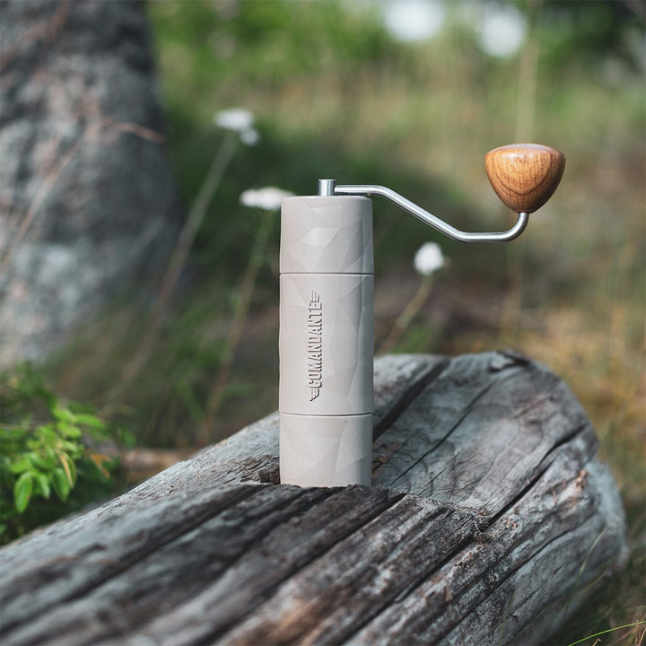 Comandante X25 Trailmaster Dune Coffee Grinder with a wooden handle on a wooden log outdoors