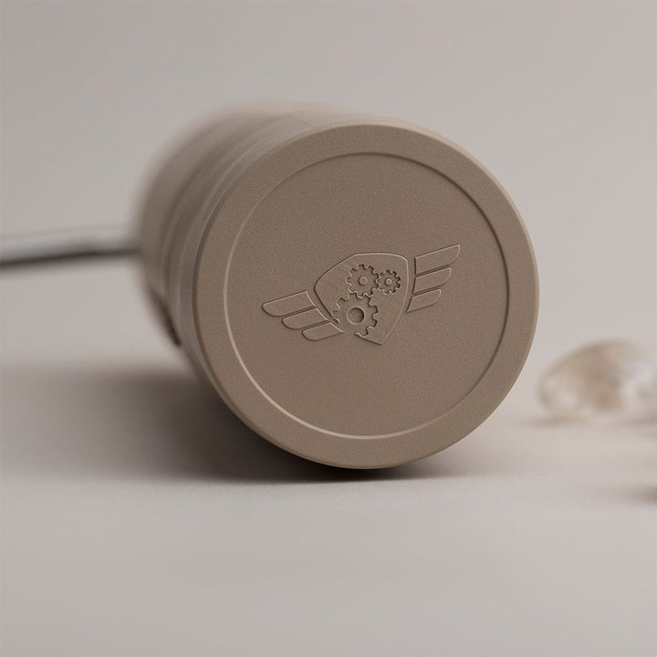 Close-up of a Comandante X25 Trailmaster Dune Coffee Grinder with the Comandante logo on a light background