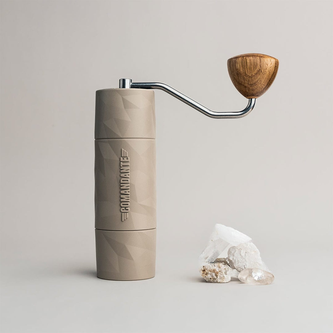 Comandante X25 Trailmaster Dune Coffee Grinder with wooden handle alongside some sweet confectionery on a light grey background