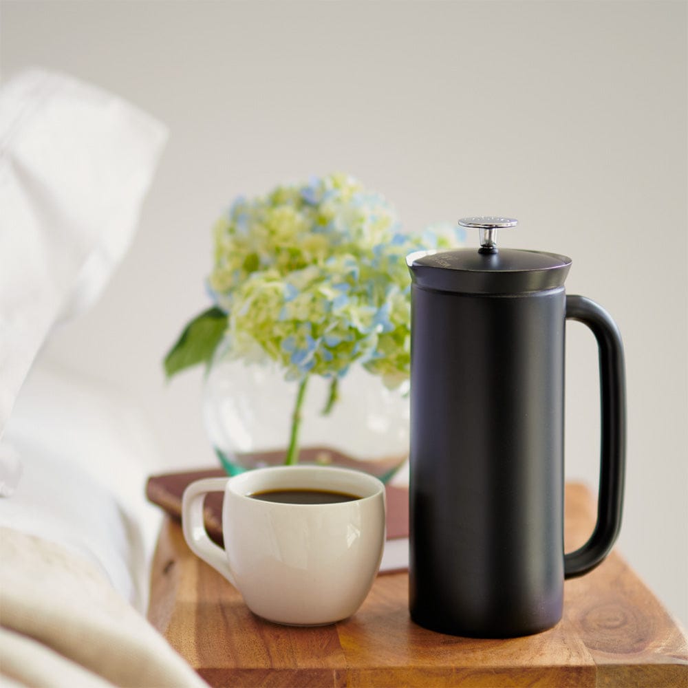 A Black ESPRO P7 French Press Coffee Maker and a white mug with coffee on a wooden tray with flowers in the background