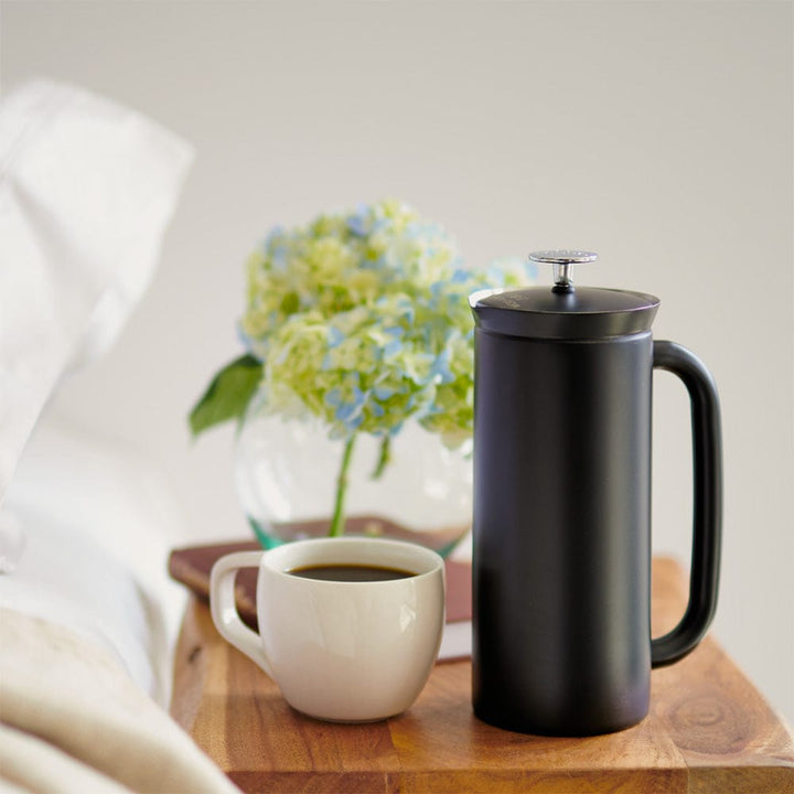 A Black ESPRO P7 French Press Coffee Maker and a white mug with coffee on a wooden tray with flowers in the background