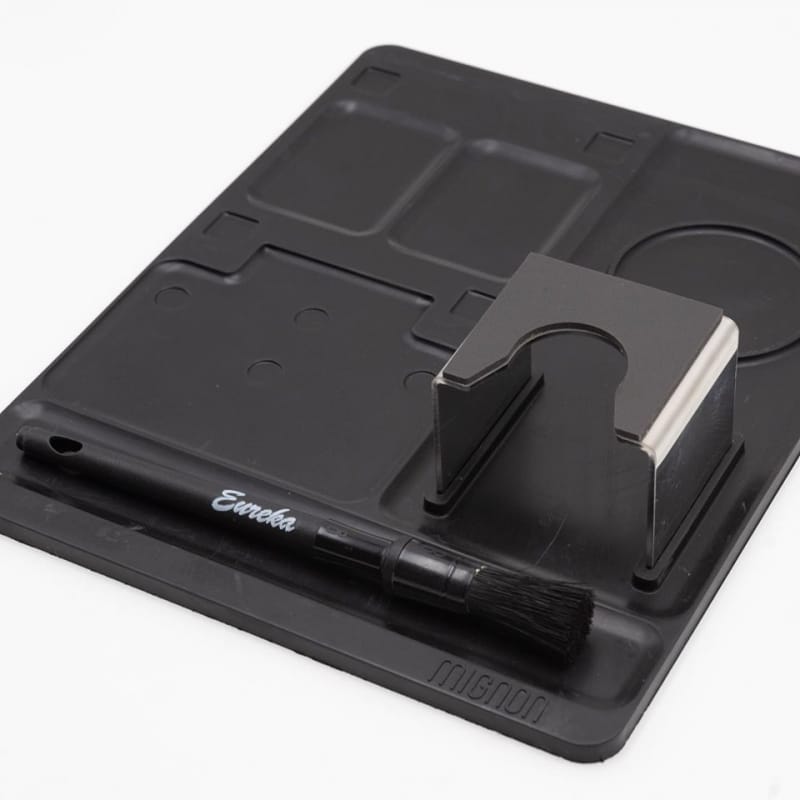 Eureka Oro Mignon XL 65 Coffee Grinder Mat with cleaning brush and tamp bay on a white background