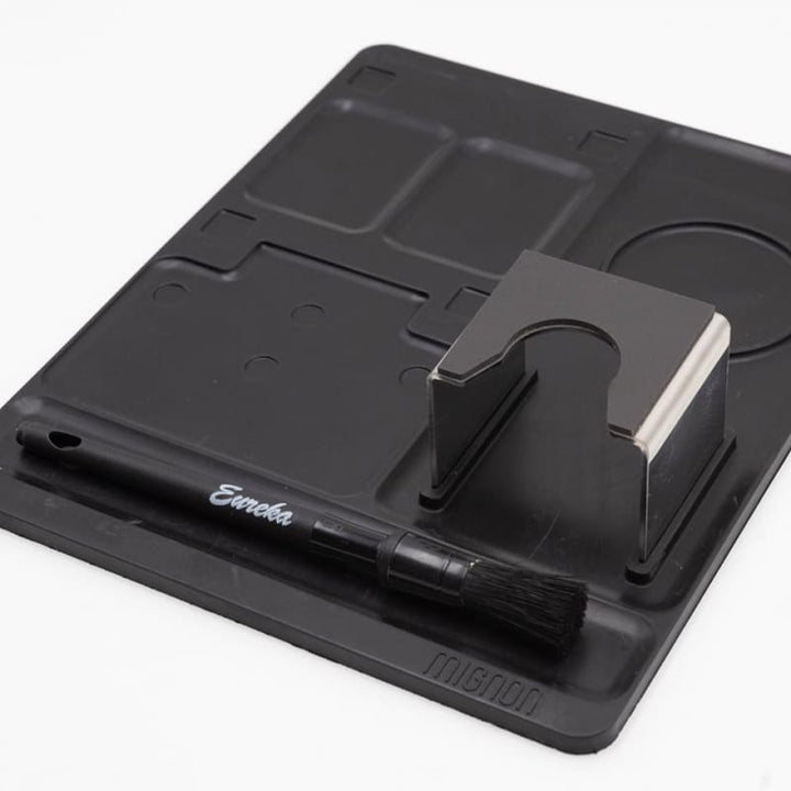 Eureka Oro Mignon XL 65 Coffee Grinder Mat with cleaning brush and tamp bay on a white background