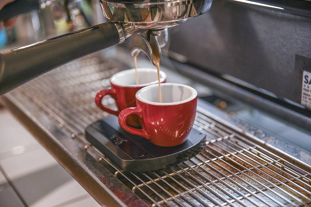 Espresso shot pouring into two red cups from a coffee machine on a Felicita Arc Waterproof Coffee Scale