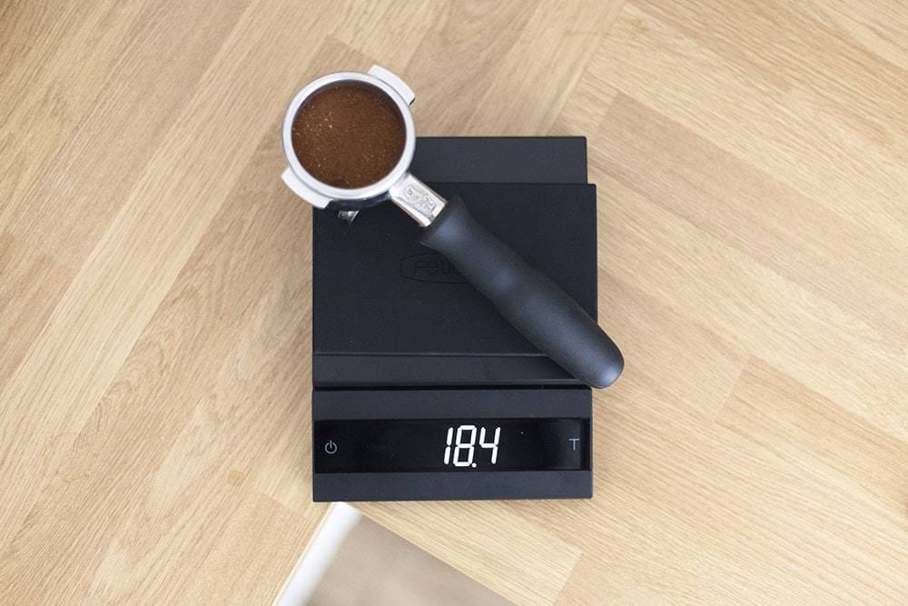 Felicita Parallel Coffee Scale in Black with a coffee handle portafilter on a wooden surface