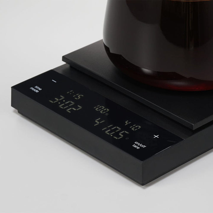Hario Polaris Coffee Scale in Black with a coffee cup on a light grey background