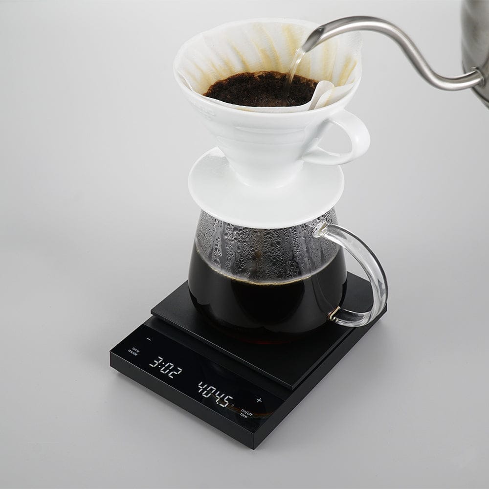 Coffee brewing process with a white pour-over coffee filter and glass carafe on a Hario Polaris Coffee Scale in Black.