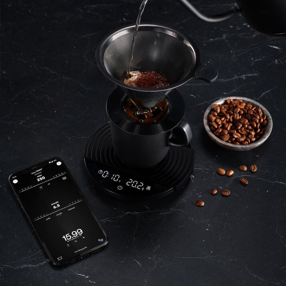 Coffee brewing process with a Black Wilfa Uniform Coffee and Kitchen Scale, phone app, and coffee beans on a dark surface.