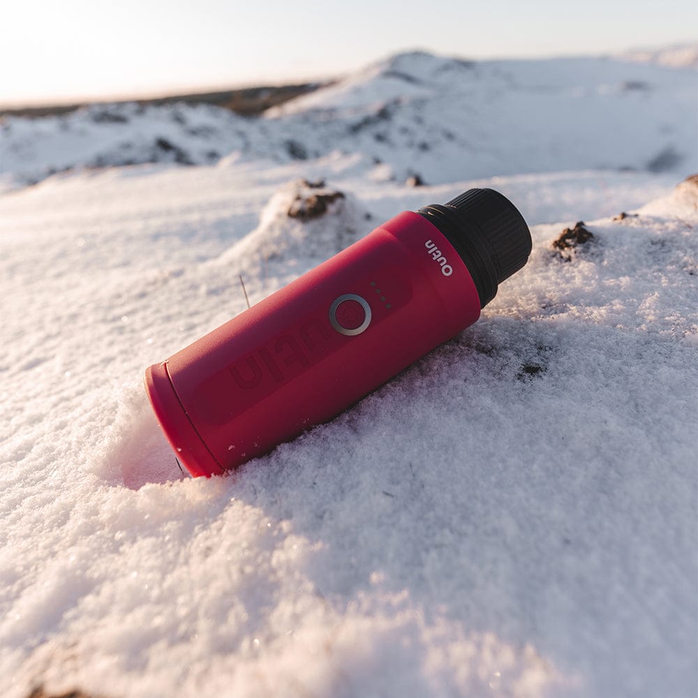 OutIn Nano Portable Espresso Coffee Machine in Fuchsia Pink lying on a snowy surface