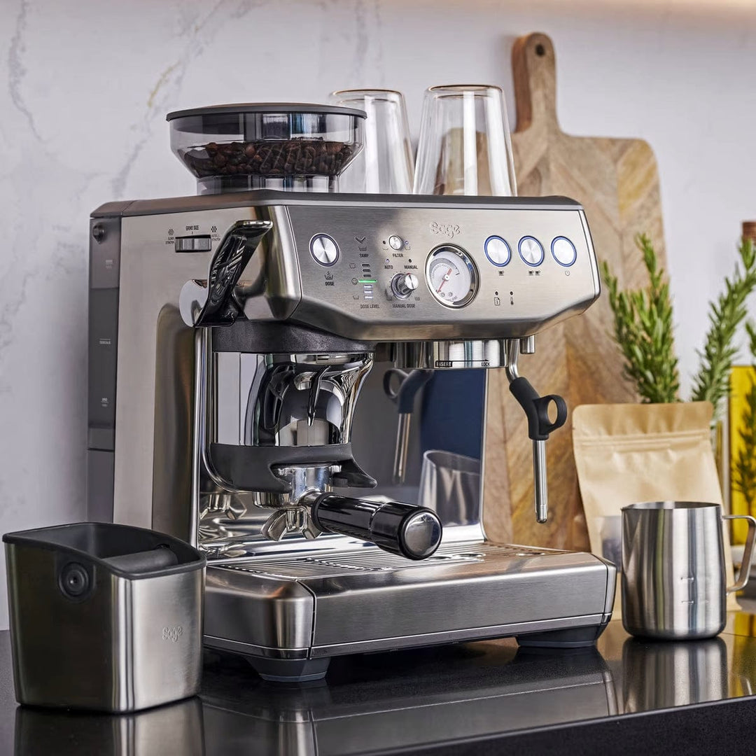 Stainless steel Sage Barista Express Impress Espresso Machine on a kitchen counter with various items in the background.