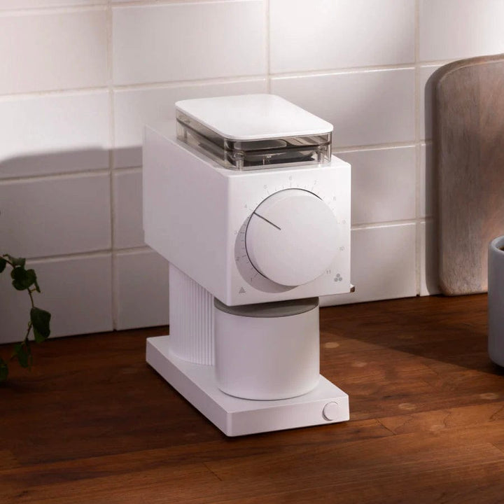 White Fellow Ode Gen 2 Electric Coffee Grinder on a wooden floor with a tiled wall background
