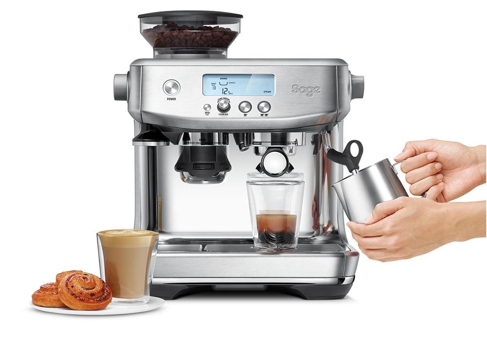 The Sage Barista Pro Espresso Machine in Stainless Steel with a glass of coffee and a hand holding a cup.