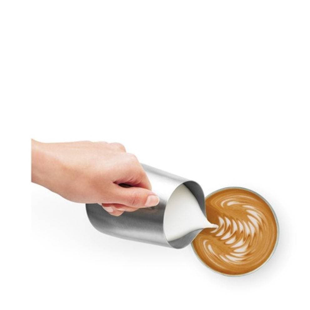 Hand pouring steamed milk into a cup of coffee with latte art on a white background