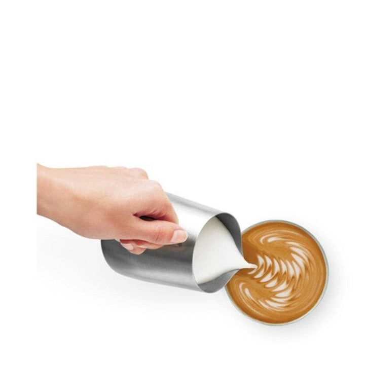 Hand pouring steamed milk into a cup of coffee with latte art on a white background